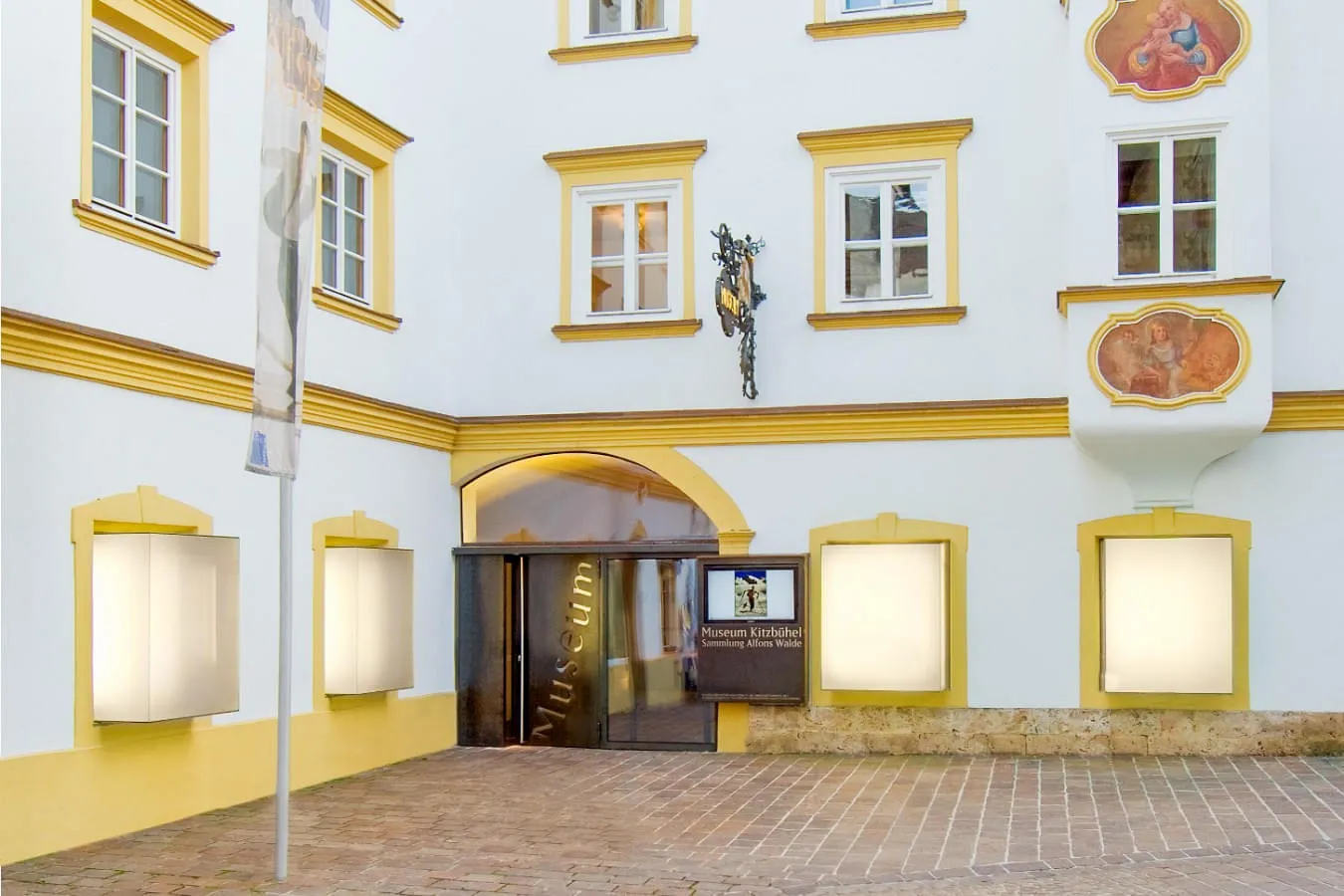 Hausfassade des Museum Kitzbühel im Stadtzentrum mit gelben Fensterrahmen und dem Eingangstor in der Hinterstadt Kitzbühel. 