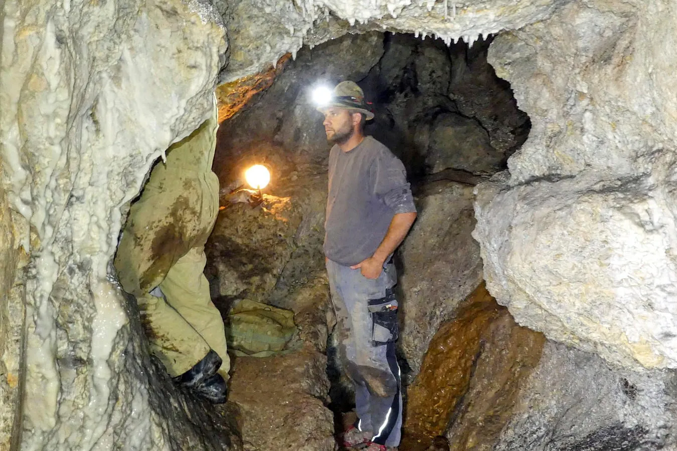 Zwei Bergarbeiter im Inneren eines Stollens in Fieberbrunn, beleuchtet von einer Lampe. 